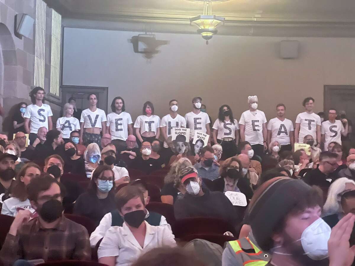 La gente usa camisetas para leer, "guardar asientos," Durante un encuentro comunitario realizado en el Teatro Castro en 2022. 