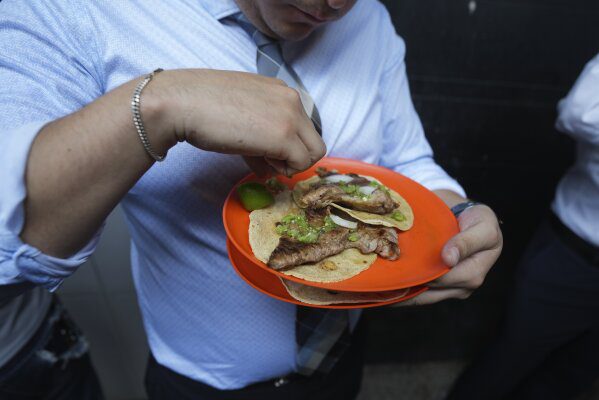 Un cliente termina de exprimir jugo de limón en sus tacos en Tacos El Califa de León, en Ciudad de México, el miércoles 15 de mayo de 2024. Tacos El Califa de León es el primer puesto de tacos en recibir una estrella Michelin de la guía gastronómica francesa.  (Foto AP/Fernando Llano)