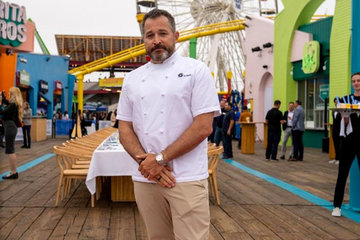 James Kent se encuentra en el muelle de Santa Mónica, con restaurantes y atracciones detrás de él.